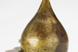 Sturmhaube, Shishak, osmanisch, um 1600 Tombak vergoldet. Hohe, konische Helmglocke mit aufgesetzter Spitze. Eingenieteter Augenschirm mit Ziernieten. Wangenklappen und Nasale fehlen. Helm und Augenschirm graviert, Kartuschen mit arabischen Inschriften und stilisiertem floralem Dekor. Rechte Stirnseite mit Marke des Arsenals in der Hagia Eirene, Konstantinopel. H 30 cm CHF 50‘000 / 80‘000 bzw. EUR 41‘650 / 66‘650