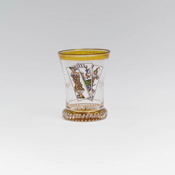 Anton Kothgasser (Wien 1769–1851 Wien) Ranftbecher mit Trull Wien, um 1820 farbloses Glas, z.T. gelbgebeizt, Gold- und Emailmalerei; geschlägelter Ranft mit gelb gebeiztem, geschliffenen Bodenstern, über dem Ranft ein Goldband; leicht konischer Becher, frontseitig die „Trull“ des Tarockblattes gemalt, auf der Rückseite in Goldschrift „Leur union est notre force“; Mundrand vergoldet, darunter gelbgebeiztes Band mit Goldblättchenbordüre; H. 11,3 cm