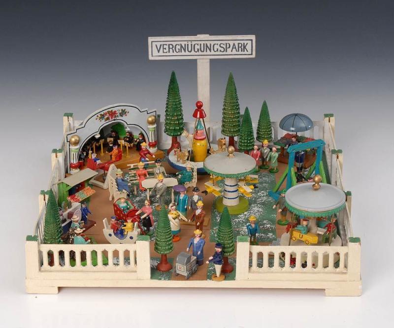 Kleiner Vergnügungspark Erzgebirge. Um 1925/30. Holz, farbig gefasst. Flache, umzäunte Platte mit verschiedenen Miniaturfiguren, Karussells, Marktständen und Konzertmuschel mit Musikern. Kat.Nr. 1052, Limit: 390 €