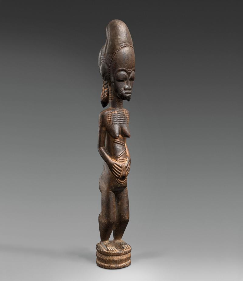 A BAULE FIGURE  Ivory Coast  The standing female with hands on the abdomen, the coiffure with tall top knot and three plaits, keloids on face, neck and body, on circular base, dark glossy patina.  43 cm. high Provenienz  Christie’s London, 7 July 1982, lot 19.  Schätzpreis: €15.000 - €20.000, Ergebnis: 40.000