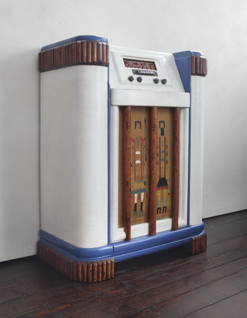 Lot 2 Thomas Molesworth An Important and Rare Radio from Ragner Ranch, Pennsylvania fir, original white and blue leather, half-pole trim, Bakelite, painted metal, clear glass, textile with two hand-painted Native American "Yei" figures 38x293/4 x15in.(96.5x75.6x38.1cm) circa 1942 Estimate $20/30,000