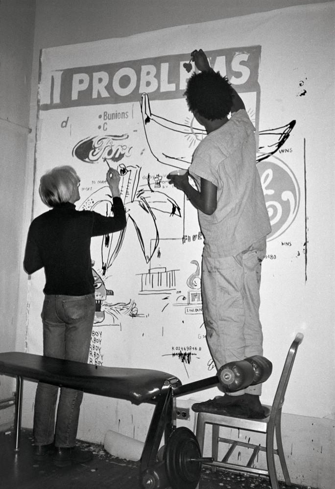 Andy Warhol and Jean-Michel Basquiat working on a Collaboration painting in Warhol’s Manhattan loft, 1984. Art © 2024 Andy Warhol Foundation for the Visual Arts / Artists Rights Society (ARS), New York