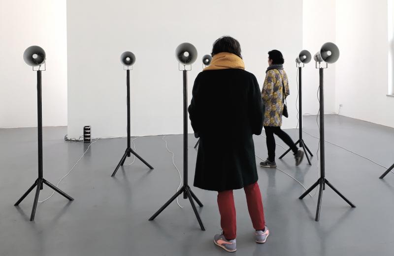 Anna Schimkat (*1974), Leipzig Brot und Ro-sen, 2019 - 20/2023 Museum Nienburg/Weser 9 Kanal-Klanginstallation mit Fahne (Chorgesang, 9 Stahlstative mit Druckkammerlautsprechern, WavePlayer 8, Digital Verstärker, bedruckte Fahne 5m x 1m,Fahnenhalter) & Publikation mit Schallplatte Maße variabel, dem Raum angepasst Höhe ca. 3,50 m x 5 m x 6 m